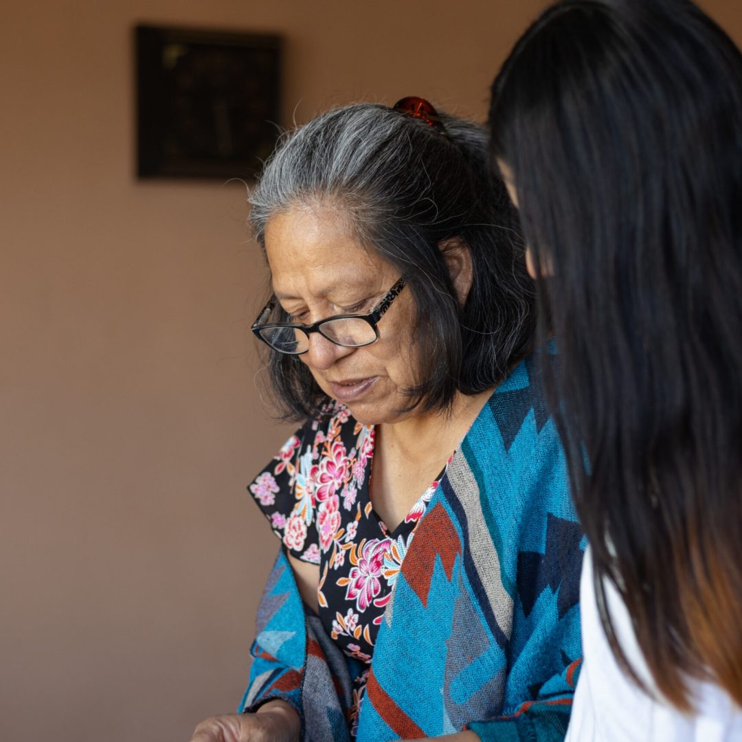 Older woman with glasses and gray hair who is a mother to her 20 year old daughter, they are cooking together sharing their learning while standing in their Mexican kitchen